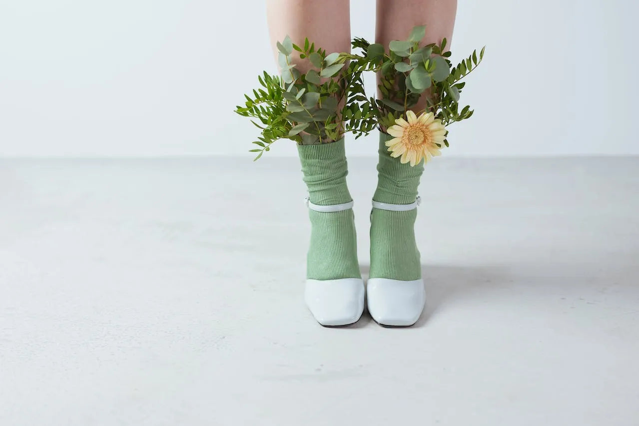 Frauenbeine in weißen Schuhen und grünen Socken in denen Blumen stecken