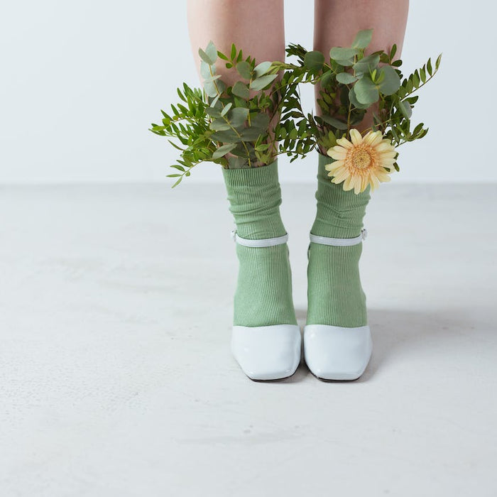 Frauenbeine in weißen Schuhen und grünen Socken in denen Blumen stecken