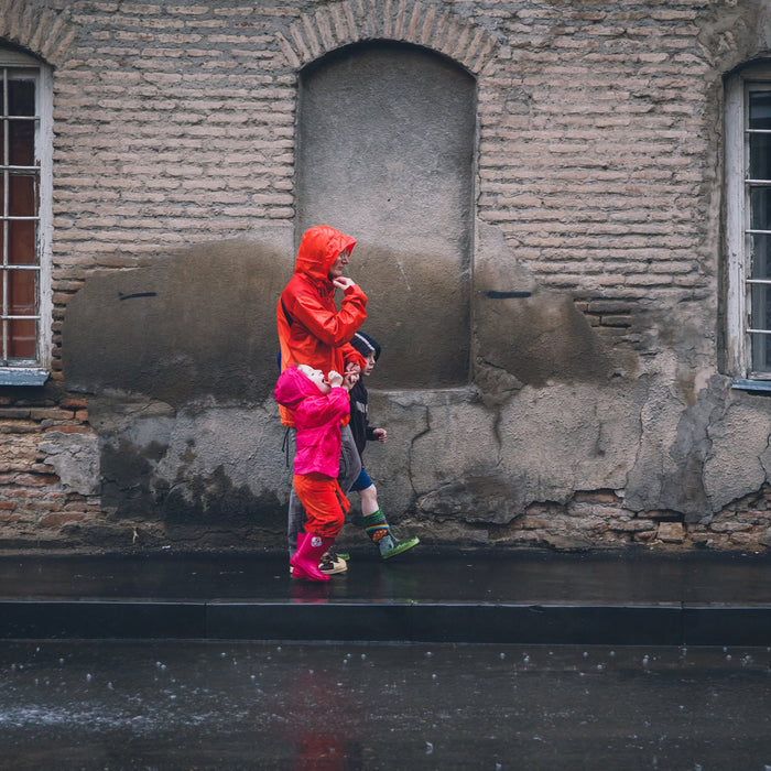 Vater mit zwei Kindern in roten Regenjacken auf Straße im Regen