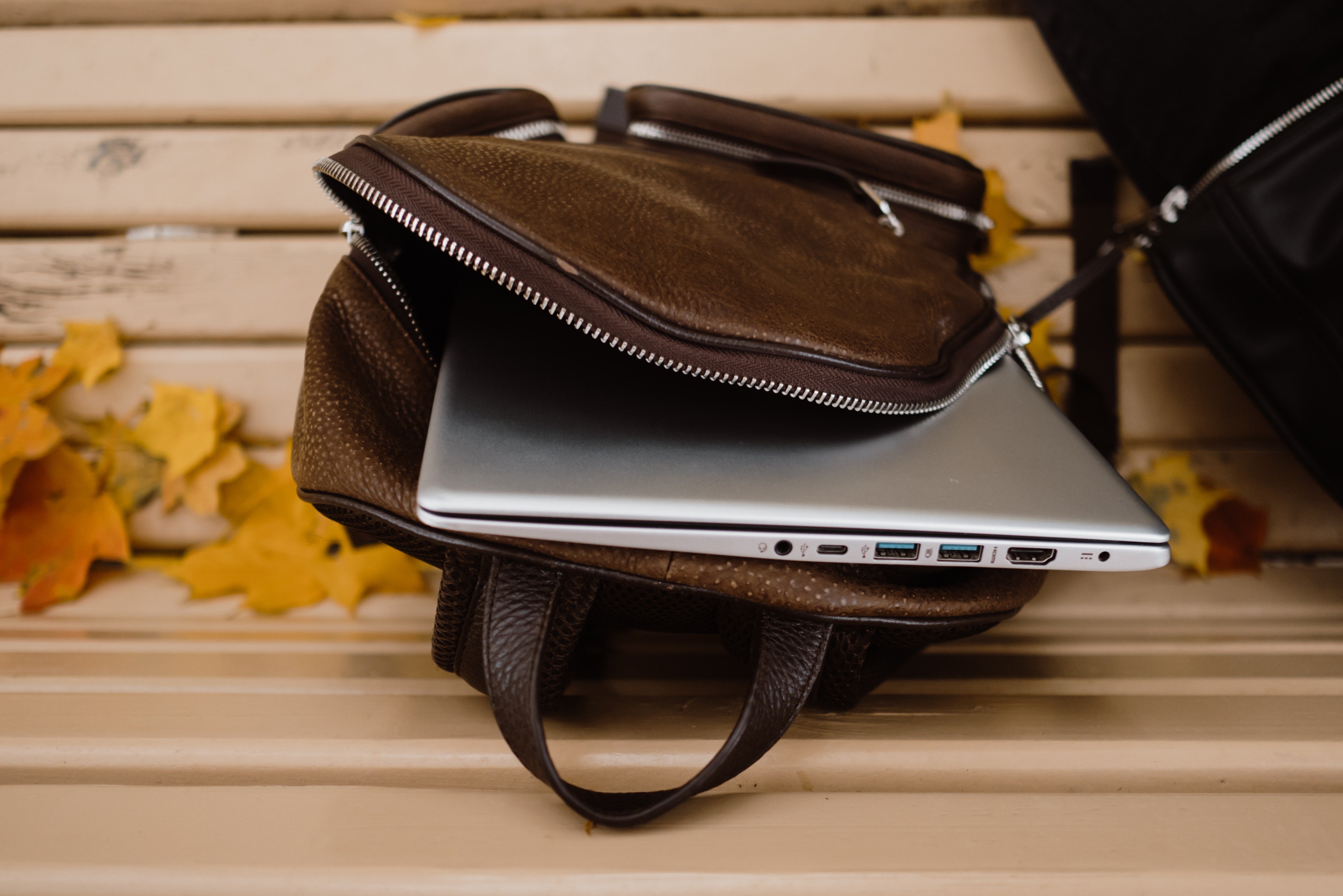 Braune Ledertasche auf Parkbank, aus der Laptop herausschaut