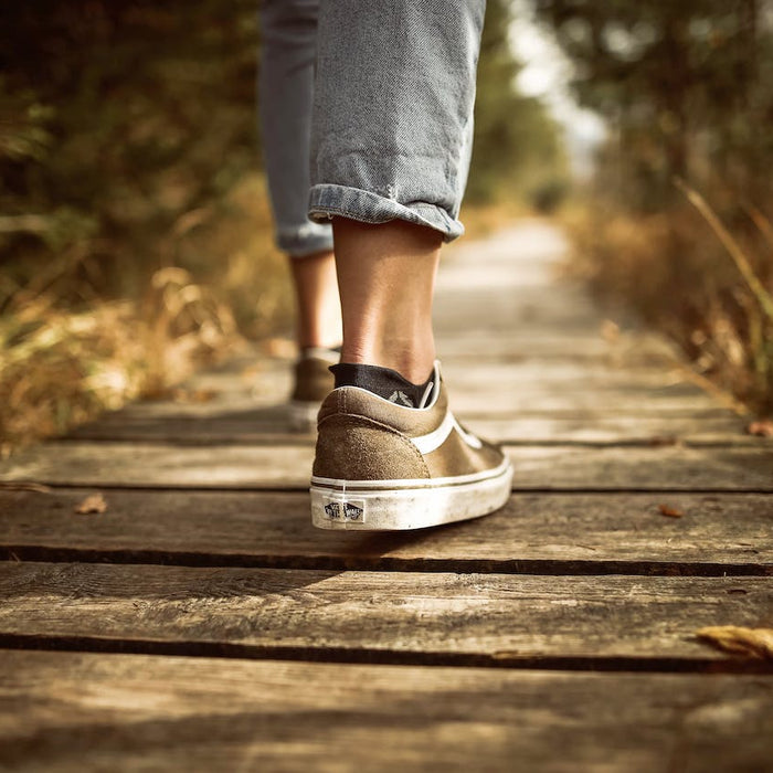 Person in Sneaker, die auf einem Holzweg in Natur spazieren geht